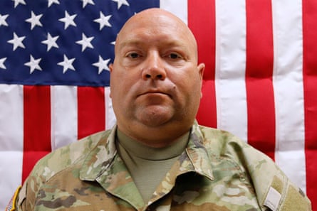 a man a soldier’s uniform stands in front of a US flag