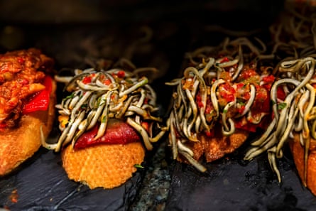 A food display of snacks made up of bread with baby eel and vegetables on top