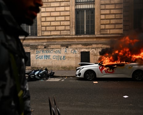 In Paris, a white car burns on a street beside graffiti reading "introduction to civil war"