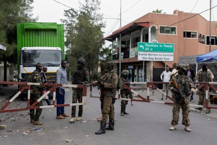 Six men in combat gear patrol a gated entrance to a street