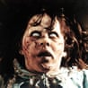 Regan, from The Exorcist, with pale scarred skin and white eyes, stares upward