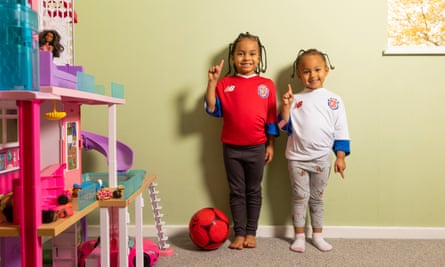 Zion and Siara Williams Monge wearing red and white Costa Rica World Cup shirts and standing against a wall in their bedroom with a football beside them and a large doll’s house to one side