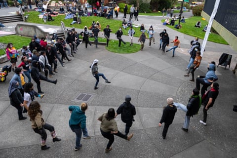 A circle of protesters follow a dance led by someone in the middle