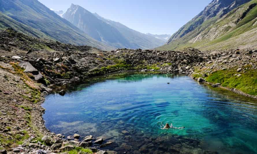 Someone swimming in a turquoise rock pool, mountain peaks behind