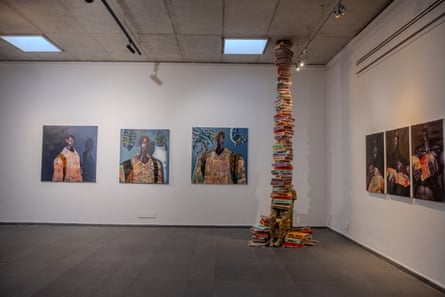 Sebuah ruangan putih dengan gambar di dinding dan tumpukan buku setinggi langit di sudut