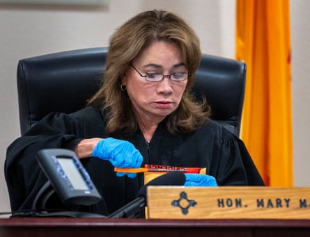 woman in judge’s robe uses scissors to open package while wearing latex gloves