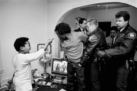 Police officers restrain a man in a family home while a young boy points a finger at him