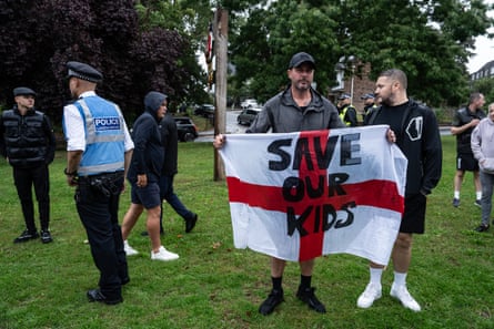 A man stands holding an England flag with ‘save our kids’ written in bold black letters across it