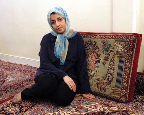 Narges Mohammadi wearing a light blue headscarf and dark clothing sits on an ornate patterned carpet.