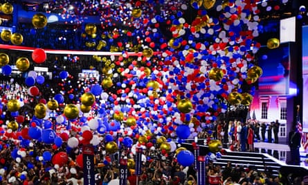 huge number of red, white blue and yellow balloons pour over crowd as several people stand on stage