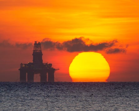 The sun rises over the sea beside a silhouetted oil platform moored off Kirkcaldy