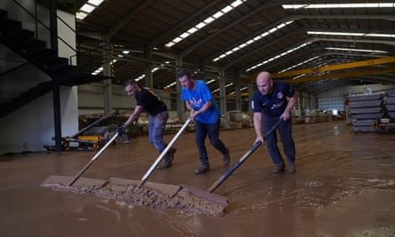 People sweep mud from a warehouse in a flood damaged area in Chiva.