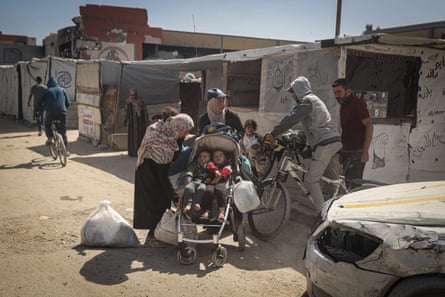 Young men on bicycles and women with a pushchair holding two children outside temporary shelters