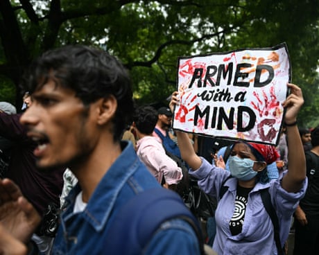 A person holds a handmade placard reading 'ARMED with a MIND' at a crowded outdoor protest