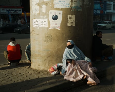 People sitting next to a large pillar on a road.