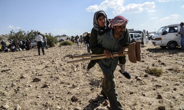 A Syrian Kurd man carries a woman with crutches across the border into Turkey
