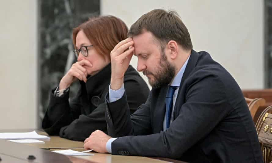 Nabiullina and a young man sitting looking down at a table, with Nabiullina holding her chin in her hand