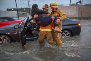 A firefighter carries a woman from her car after it was caught in street flooding in Sun Valley, California.