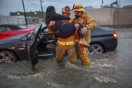 A firefighter carries a woman from her car after it was caught in street flooding in Sun Valley, California.