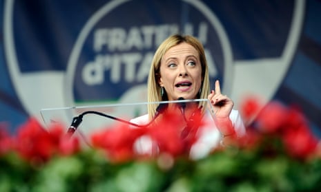 Brothers of Italy leader Giorgia Meloni speaking and holding up her finger with flowers in the foreground and a Fratelli d'Italia logo in the background