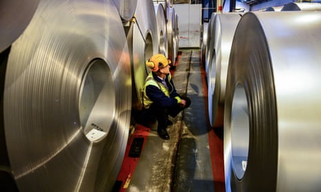 a manager stands among huge rolls of steel plate