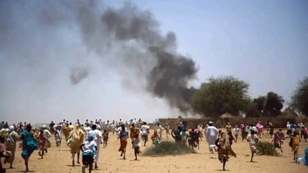 Crowds of people run across a desert plain towards plumes of thick black smoke rising from what appear to be straw huts