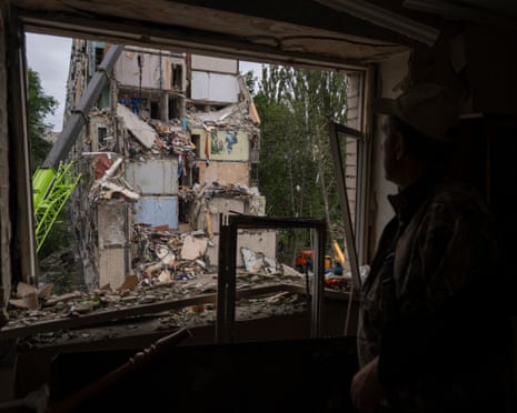 A local resident looks out of a broken window as Ukrainian rescuers work among the rubble of a destroyed residential building following an air attack in Kyiv.
