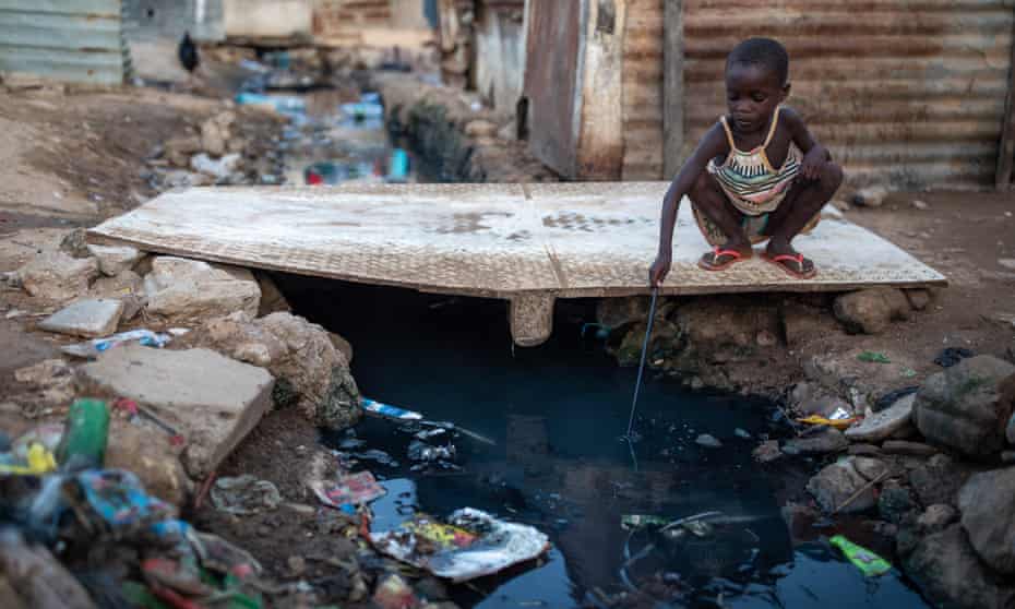 A young girl fishes waste out of a stream of sewage inside the Povoado slum in Luanda, Angola