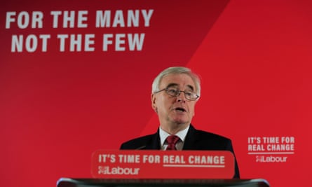 John McDonnell stands at a lectern in front of a red backdrop