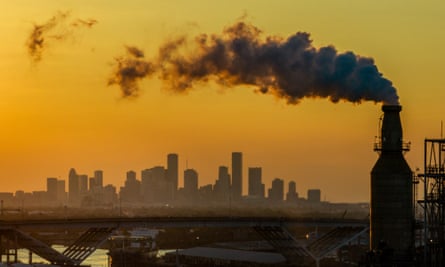 Smoke rises from the Valero Houston refinery against a yellow sky and the Houston, Texas skyline in the background. 