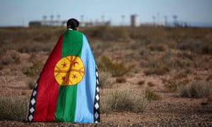 Una mujer envuelta en una bandera con instalaciones petroleras en la distancia