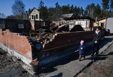 A resident and her child walk near a house destroyed by Russian shelling in the village of Moshchun.
