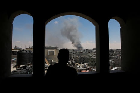 A foreground of three high, rounded window frames and a man in silhouette, with smoke rising from an urban landscape beyond him.