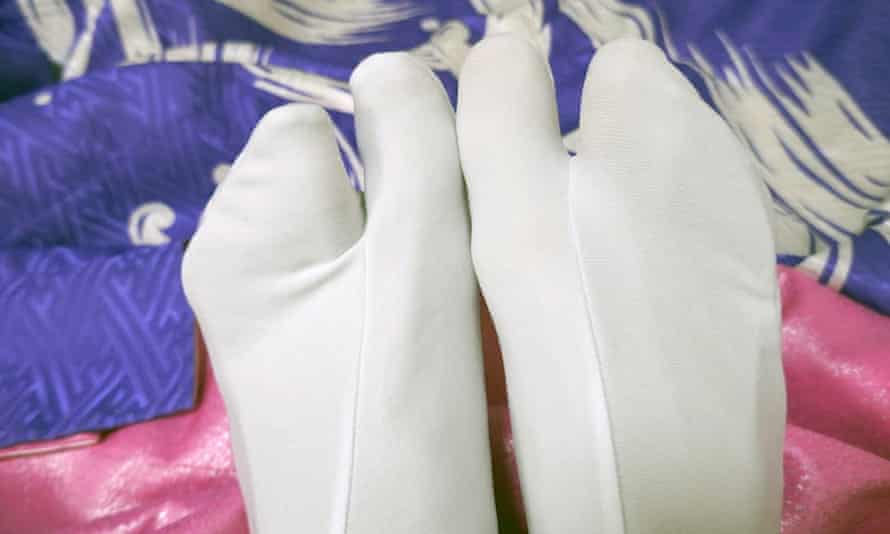 Close up image of two feet wearing white geisha tabi socks, which divide the foot into two spaces, one for the big toe and the others for the remaining toes.