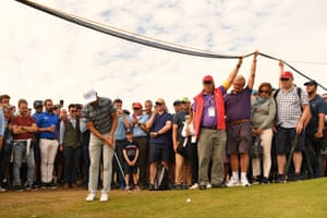 Spectators hold up television cables so that US golfer Rickie Fowler can play onto the 6th green