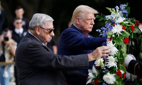 two men in suits stand while touching a wreath