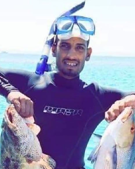 A young Arab man in a wetsuit, mask and snorkel holds up two large fish for the camera
