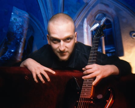 Broadrick pictured looking down at the camera, holding an electric guitar, inside a church