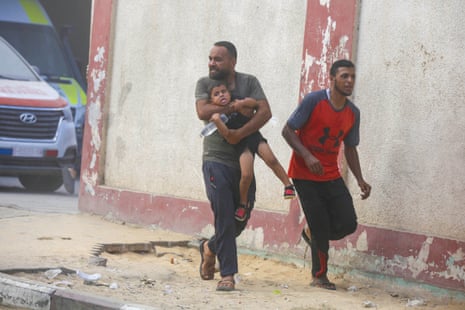 A Palestinian man holds a child and rushes to escape the area after Israeli warplanes' bomb strike on the tents where displaced Palestinians live in Deir al Balah, Gaza on August 21, 2025.
