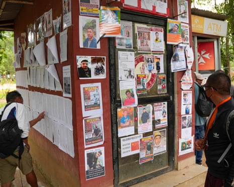 People looking a photographs and lists of names covering two walls of a cubicle