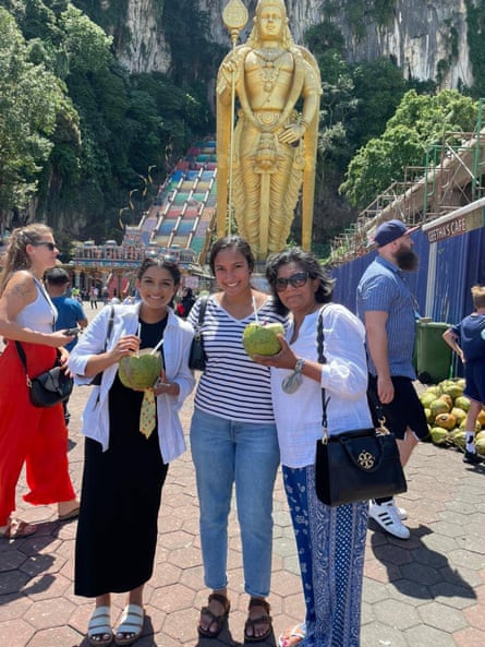 Two teenage girls and their mother pose with a coconut drink at the Batu Caves in Gombak, Malaysia.