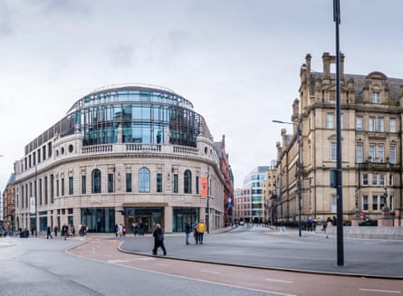 A large stone building with a carved, curving facade and a modern glass roof extension adding several floors.