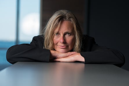 A woman in a blazer leaning on a desk with her hands under her chin