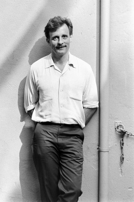 Edmund White in white shirt and dark trousers, standing by a door in London in July 1983