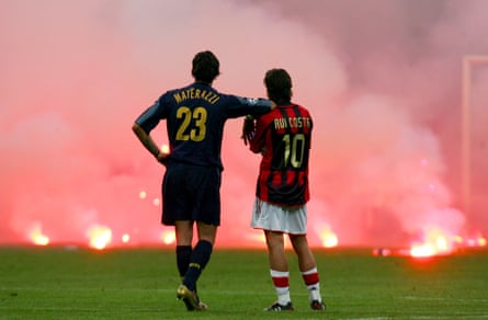 InterâÂÂs Marco Materazzi and MilanâÂÂs Rui Costa wait in arms together as supporters throw flares onto the pitch