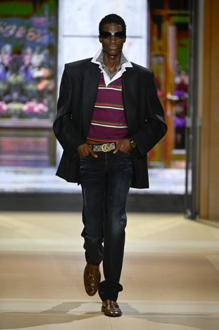 Male model wearing a black jacket, striped rugby shirt and jeans with a Gucci branded belt