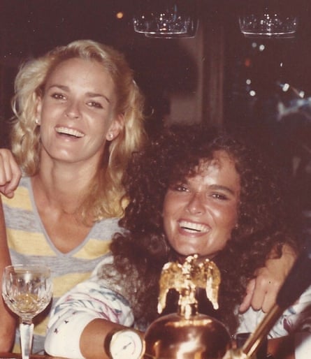 A blond woman in a yellow and blue top and a woman with brown curly hair, both smiling, with a wineglass visible
