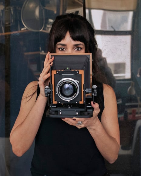 Artist Hoda Afshar holds a large vintage box camera up to her face in her studio