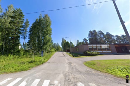 A street scene featuring a road with a pedestrian crossing of white lines, green grass and a one storey building, no cars or people, and trees