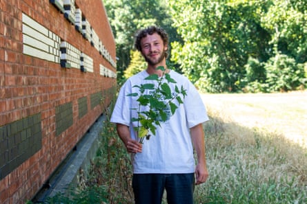 a man in a white T-shirt holding a bunch of nettles he has picked